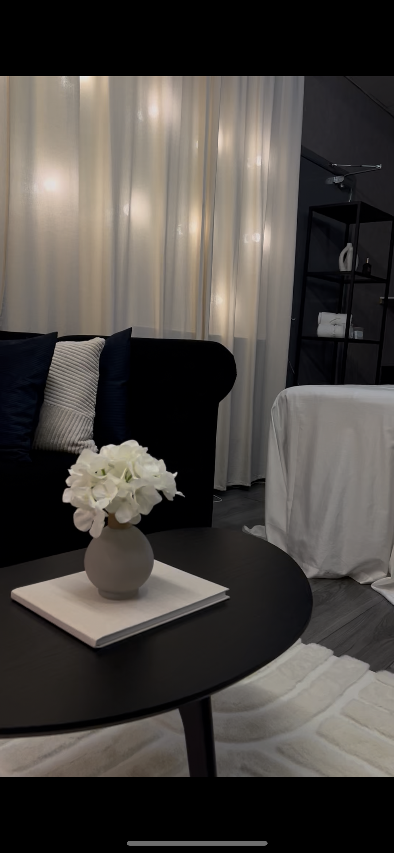 Living room with a dark sofa, round coffee table, and decorative flowers.